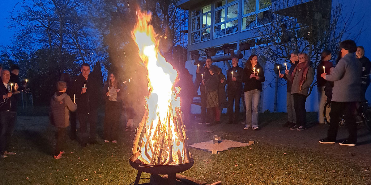 Teilnehmer*innen des Osterseminars stehen mit Kerzen in der Hand um das Osterfeuer herum