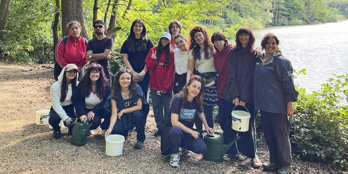 Gruppenbild: 14 Freiwillige vor einem See, sie haben Eimer und Gießkannen in den Händen